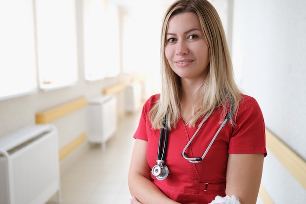 Retrato de uma jovem médica com estetoscópio em uniforme vermelho no corredor do hospital