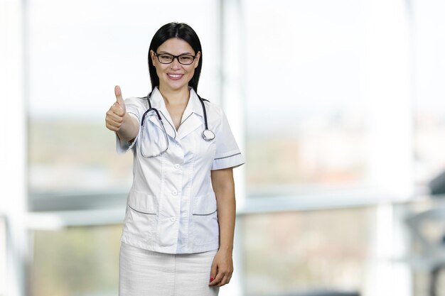 Retrato de uma jovem médica mostrando como gesto usando óculos e estetoscópio