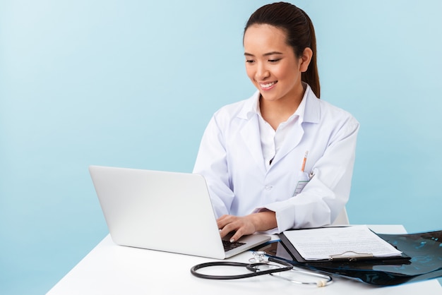 retrato de uma jovem médica posando isolado sobre uma parede azul, usando o computador portátil.