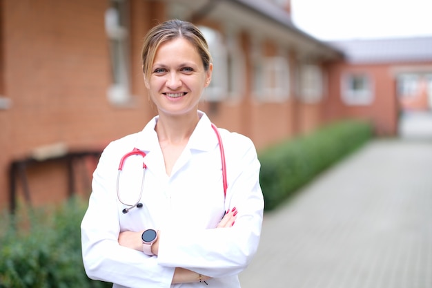 Retrato de uma jovem médica sorridente com um estetoscópio vermelho perto da clínica
