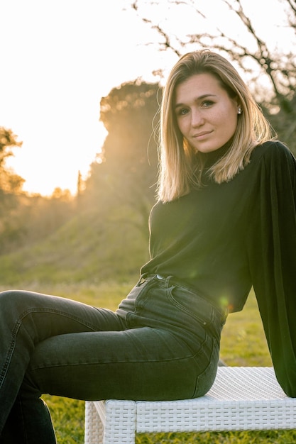 Retrato de uma jovem modelo loira vestida de preto olhando para a câmera sentada de pernas cruzadas