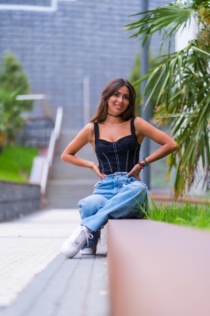 Retrato de uma jovem modelo morena em um boné preto e jeans sentado na cidade