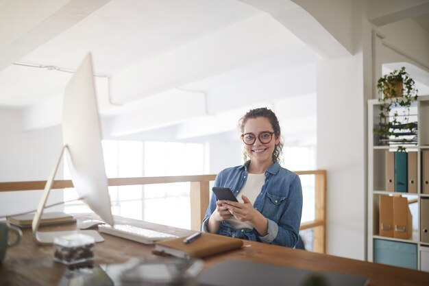 Foto retrato de uma jovem moderna usando óculos e sorrindo para a câmera enquanto está sentado no local de trabalho em um escritório branco, conceito feminino de desenvolvedor de ti, espaço de cópia