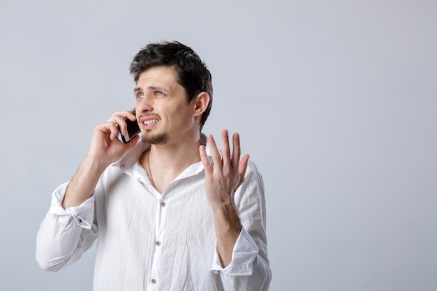 Retrato de uma jovem morena atraente com camisa branca, falando no smartphone sobre o fundo cinza.