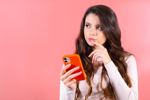 Retrato de uma jovem morena atraente e pensativa com um smartphone conversando com amigos olhando