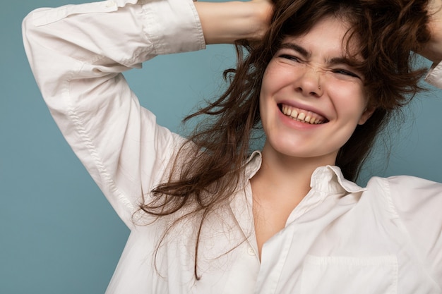 Retrato de uma jovem morena bonita positiva alegre fofa sorridente em uma camisa branca casual