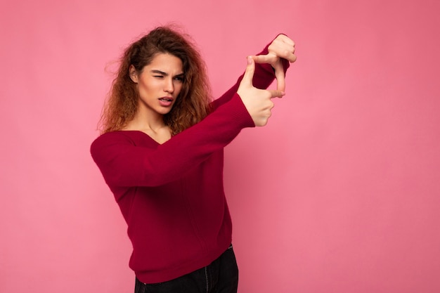 Retrato de uma jovem morena bonita positiva e encaracolada com emoções sinceras, vestindo rosa moderno