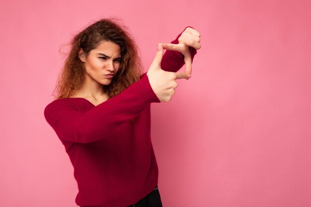 Retrato de uma jovem morena bonita positiva e encaracolada com emoções sinceras, vestindo rosa moderno