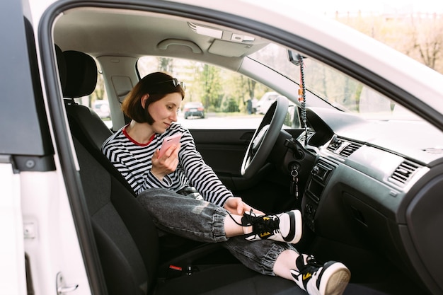 Retrato de uma jovem morena dirigindo um carro usando um smartphone
