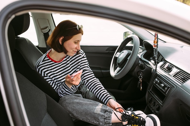 Retrato de uma jovem morena dirigindo um carro usando um smartphone