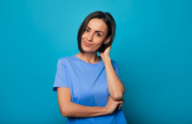 Retrato de uma jovem morena encantadora com penteado estiloso em camiseta azul enquanto ela está posando e olhando para a câmera