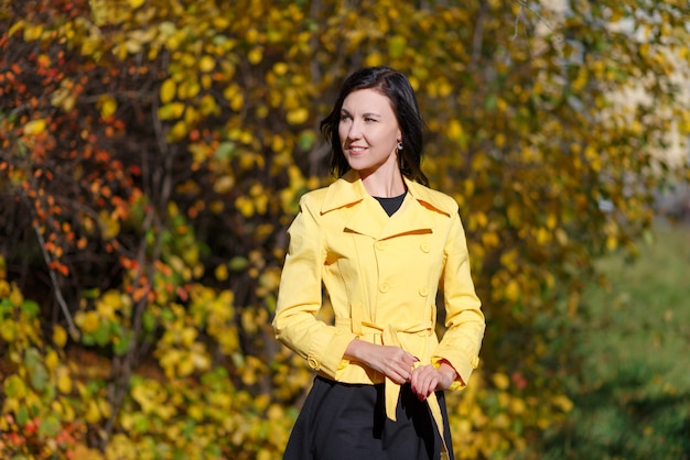 Retrato de uma jovem morena esbelta com uma jaqueta amarela em um parque.