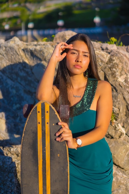 Retrato de uma jovem morena latina com um skate usando um vestido verde