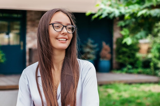 Retrato de uma jovem morena sorridente em óculos contra o pano de fundo das árvores da natureza construindo fachada