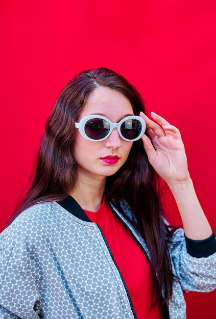 Retrato de uma jovem morena tirando os óculos de sol em fundo liso vermelho