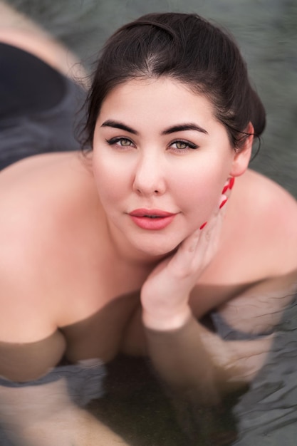 Retrato de uma jovem morena xxl em relaxamento de maiô preto na piscina no spa hot springs resort