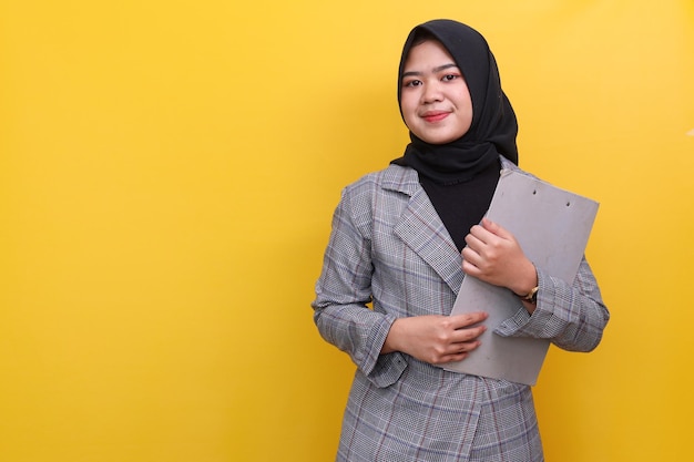 Retrato de uma jovem muçulmana asiática bem-sucedida em hijab e vestido formal, segurando a prancheta e o banheiro