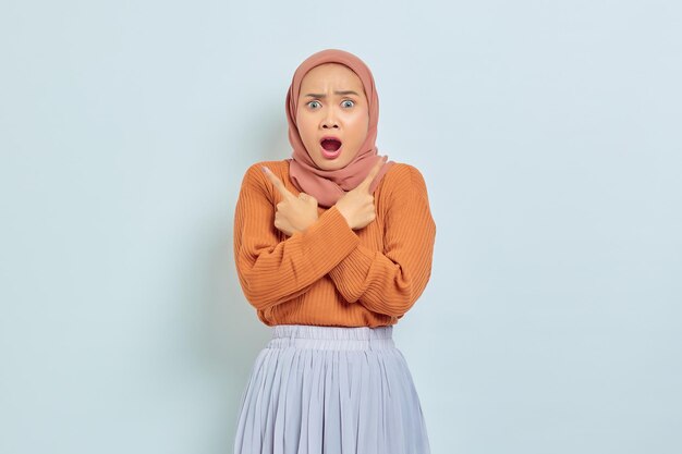 Retrato de uma jovem muçulmana asiática surpreendida com boca aberta e dedos cruzados no espaço de cópia isolado em fundo branco