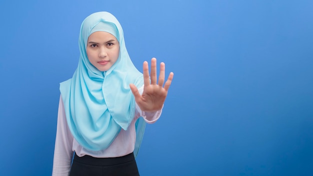 Retrato de uma jovem muçulmana com um hijab sobre uma parede azul