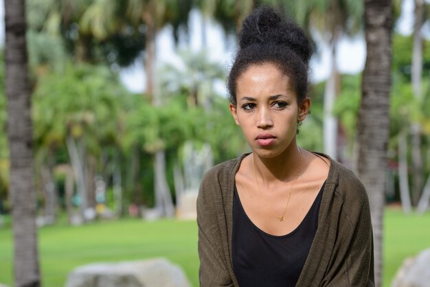 Retrato de uma jovem mulher africana bonita com cabelo afro relaxando no parque ao ar livre