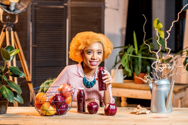 Retrato de uma jovem mulher africana com frutas vermelhas frescas e smoothies, sentado dentro de casa, no aconchegante interior de sua casa