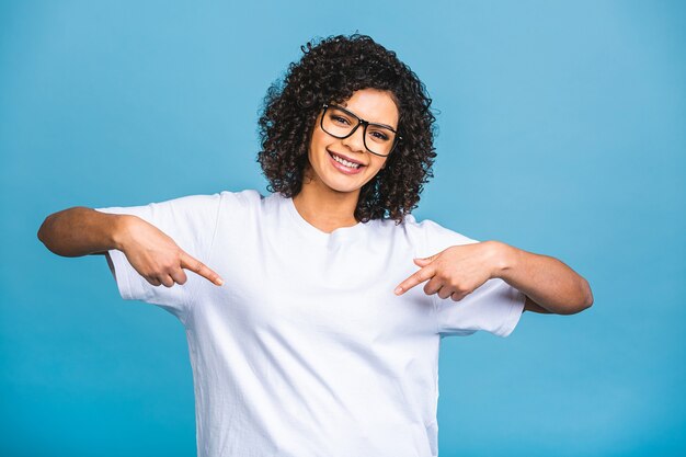 Retrato de uma jovem mulher afro-americana feliz, apontando os dedos para longe, no espaço da cópia isolado sobre o fundo azul.