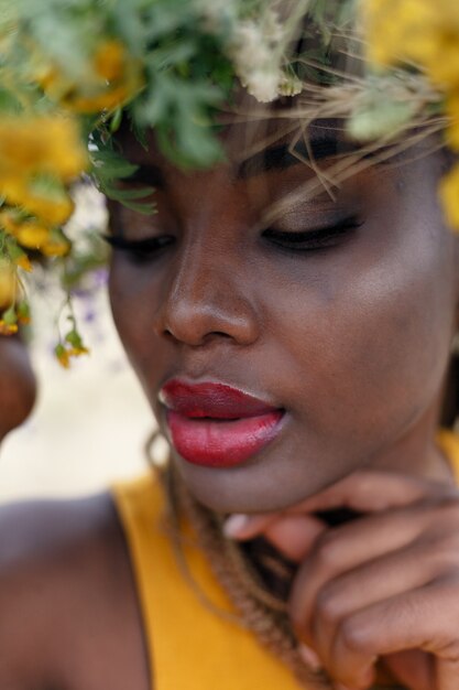 Retrato de uma jovem mulher afro-americana, modelo da moda, com grandes flores no cabelo. Retrato de uma menina em um plano torto em um campo com flores. coroa na cabeça dela