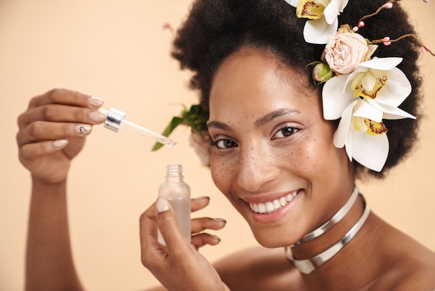 Retrato de uma jovem mulher afro-americana sardenta segurando um frasco de creme de soro facial