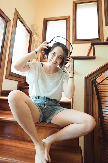 Retrato de uma jovem mulher americana hippie brincalhão em fones de ouvido sorrindo para a câmera na sala de estar em casa