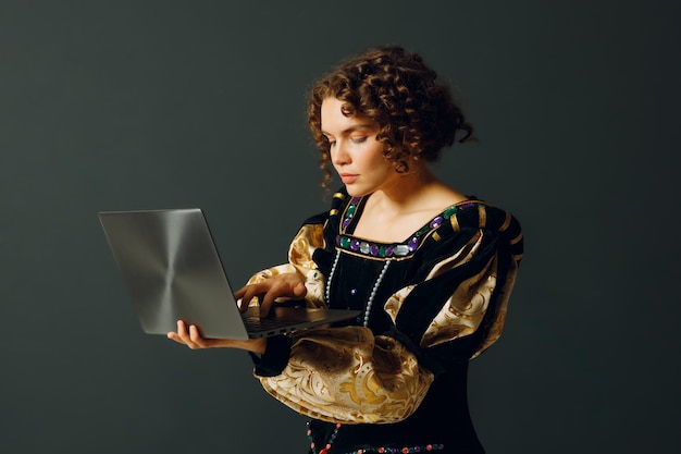 Retrato de uma jovem mulher aristocrática vestida com um vestido medieval trabalhando em um laptop