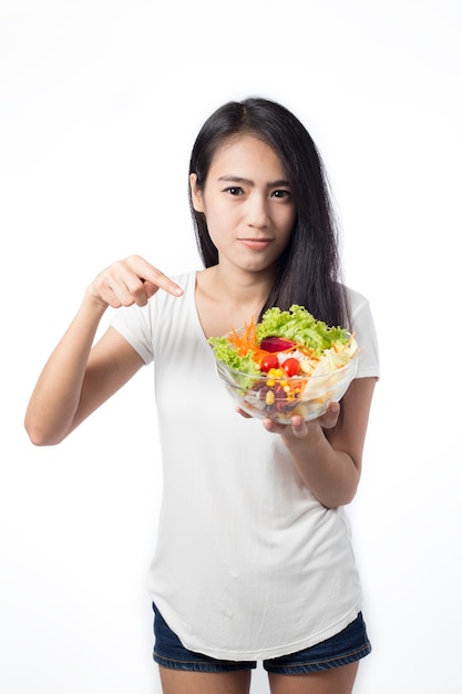 Retrato de uma jovem mulher asiática bonita comendo salada de legumes isolada no branco.