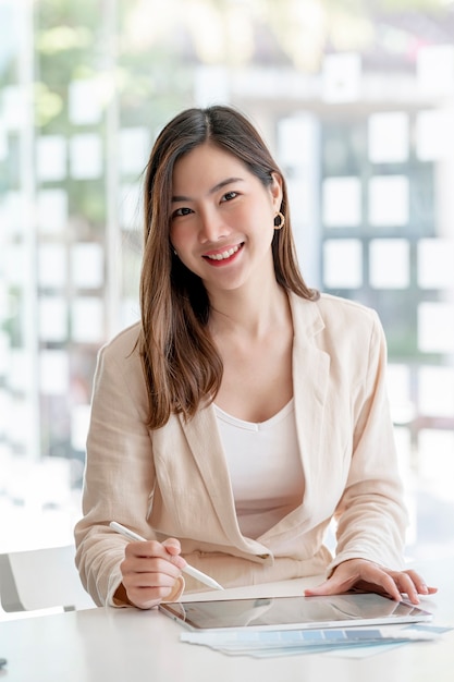 Retrato de uma jovem mulher asiática bonita, sorrindo e olhando para a câmera enquanto trabalhava no escritório.