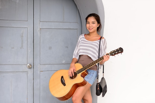 Retrato de uma jovem mulher asiática bonita tocando violão nas ruas da cidade ao ar livre