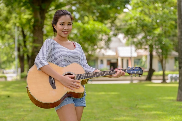 Retrato de uma jovem mulher asiática linda tocando violão no parque ao ar livre