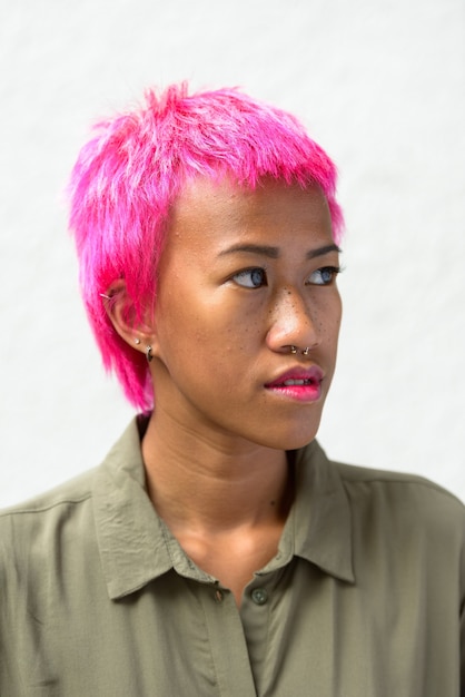 Retrato de uma jovem mulher asiática rebelde com cabelo rosa contra o espaço em branco