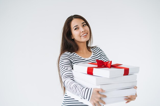 Retrato de uma jovem mulher asiática sorridente com uma pilha de caixas de presente nas mãos sobre fundo branco isolado