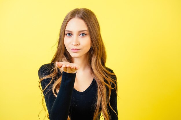 Retrato de uma jovem mulher atraente com cabelo comprido manda um beijo no ar no estúdio em um fundo amarelo. o conceito de Dia dos Namorados e a declaração de amor.