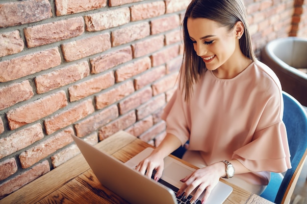 Retrato de uma jovem mulher atraente, sentado na cantina e usando o laptop