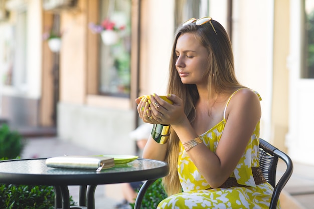 Retrato de uma jovem mulher atraente, sentado no café com uma xícara de café. Senhora bebendo chá aromático. Foto de garota bonita no refeitório esperando seu encontro.