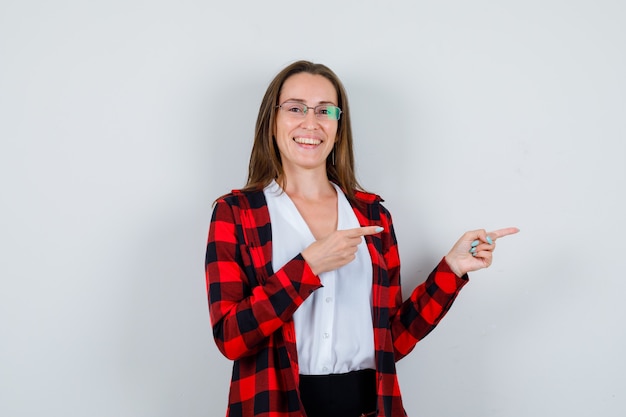 Retrato de uma jovem mulher bonita apontando para a direita em uma roupa casual e olhando de frente com alegria