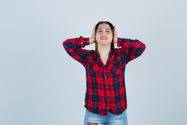 Retrato de uma jovem mulher bonita cobrindo as orelhas com as mãos na camisa casual e olhando para a frente alegre