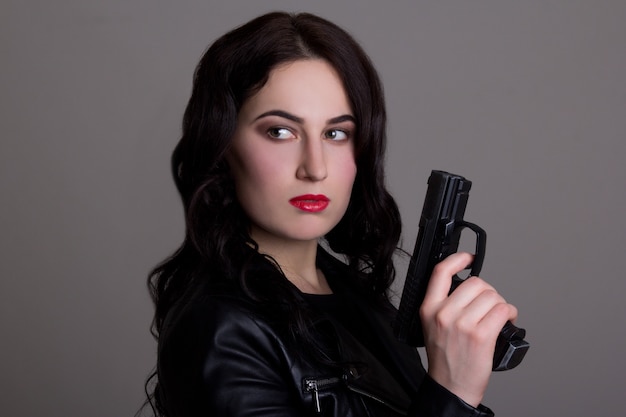 Retrato de uma jovem mulher bonita com arma sobre fundo cinza