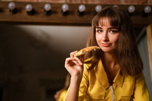 Retrato de uma jovem mulher bonita em amarelo morde uma fatia de close-up de pizza