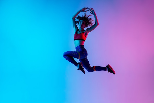 Retrato de uma jovem mulher bonita em roupas esportivas brilhantes, isolado no estúdio rosa azul gradiente