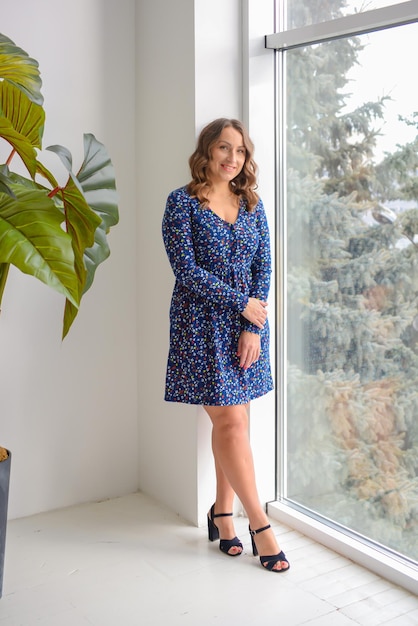 retrato de uma jovem mulher bonita em um vestido azul em um interior moderno e elegante perto da janela