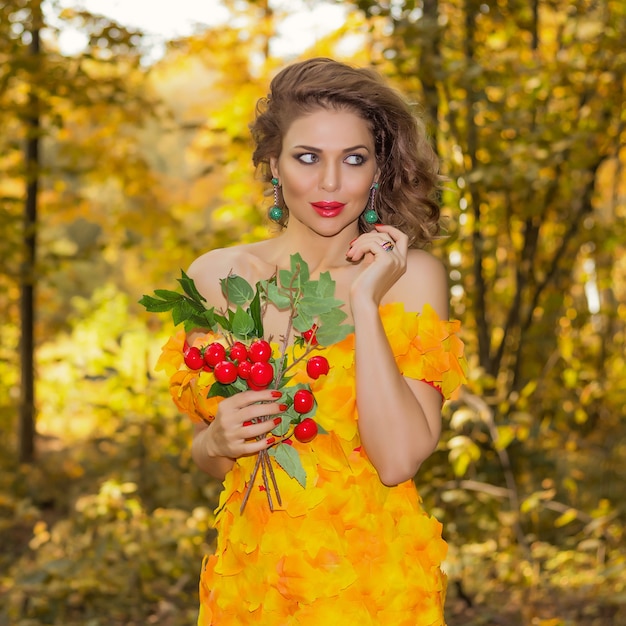 Retrato de uma jovem mulher bonita em um vestido feito de folhas de outono no parque na temporada de outono