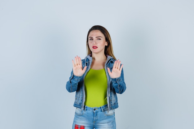 Retrato de uma jovem mulher bonita mostrando gesto de parada em roupa jeans e olhando confiante para a frente