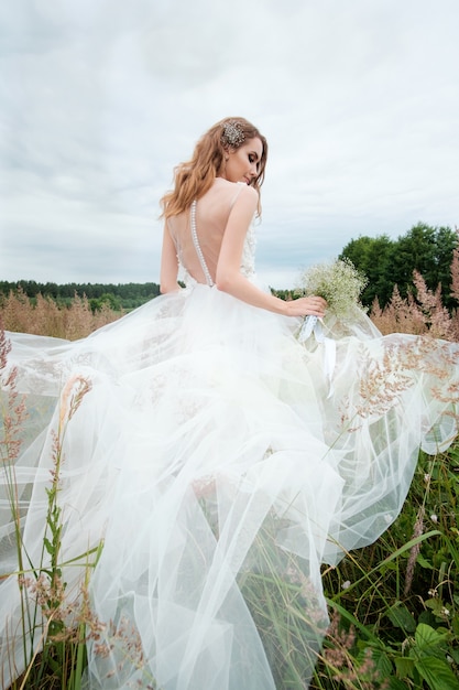 Retrato de uma jovem mulher bonita no vestido de casamento branco ao ar livre