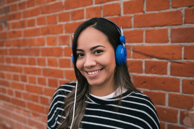 Retrato de uma jovem mulher bonita ouvindo música com fones de ouvido azuis no meio da rua.