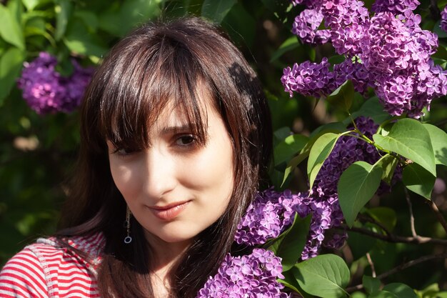 Retrato de uma jovem mulher bonita posando entre lilases florescendo. mulher entre arbustos de lilases em flor na primavera.